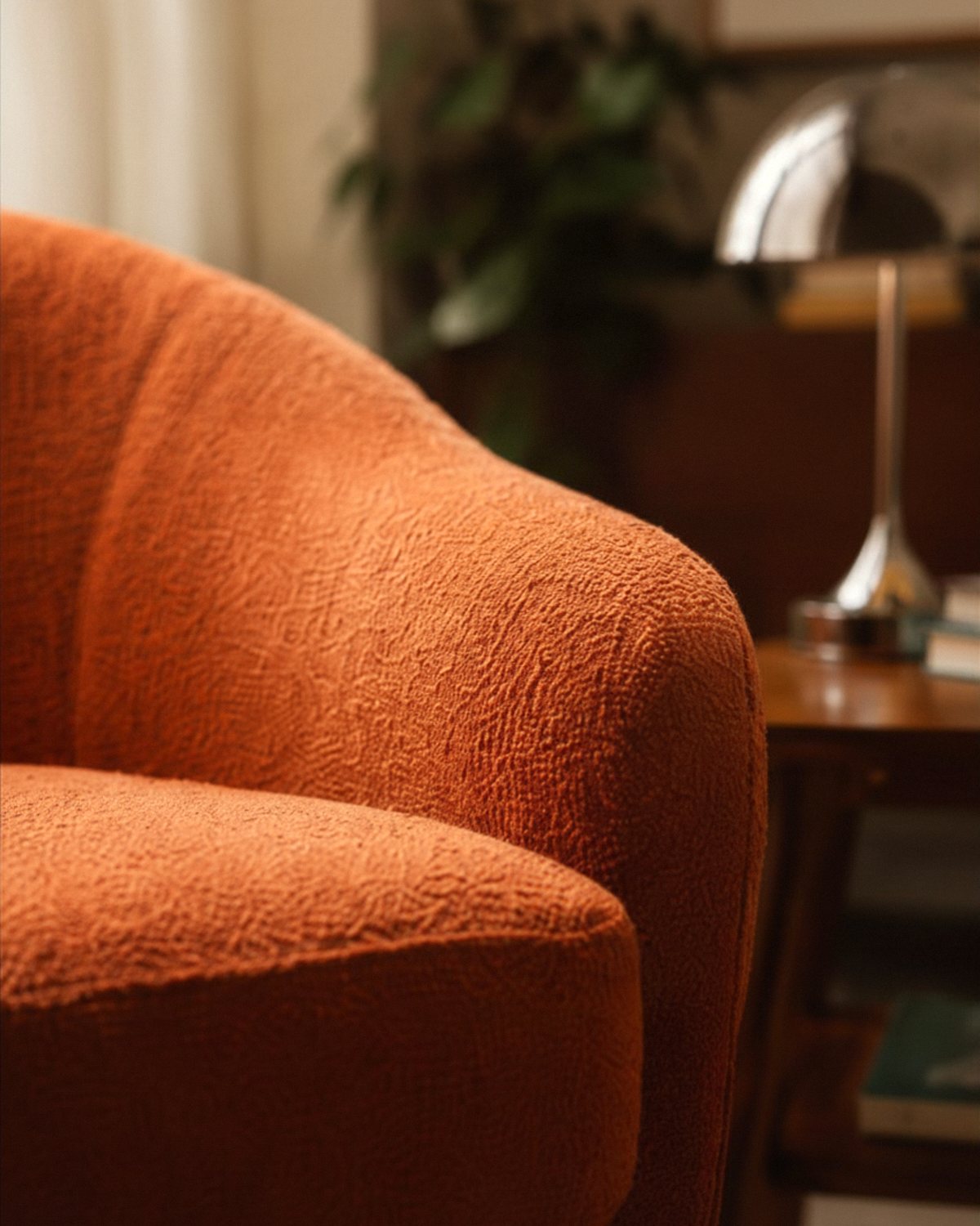 A warm terracotta bouclé chair in the Body Belonging space in Nedlands, with a soft lamp, books and a plant behind it